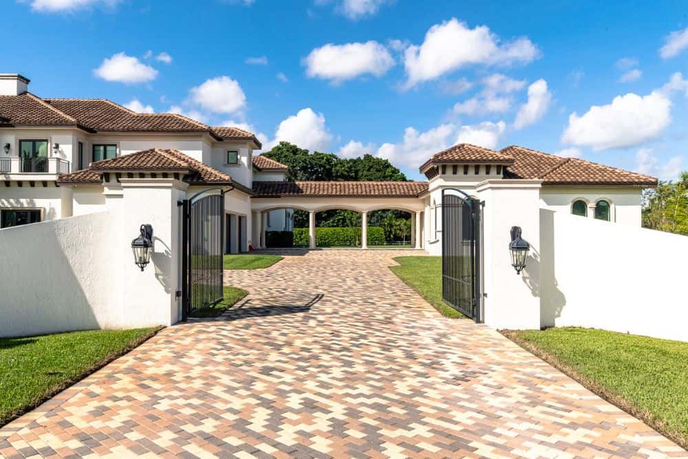 This is a close look at the outer gate of the property with a patterned driveway and black wrought iron gates.