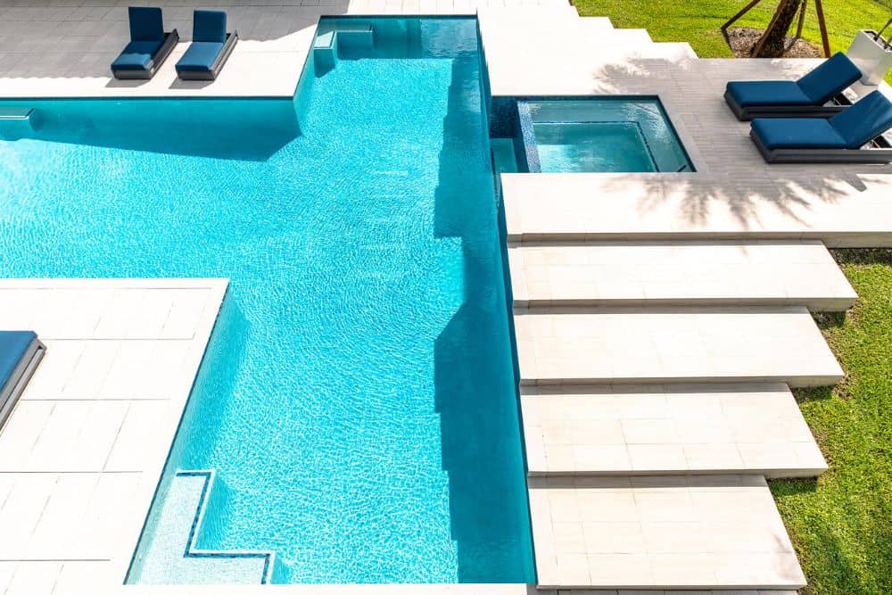 This is a top view of the swimming pool of the property with elegant geometric structures made of concrete contrasted by the grass lawn.