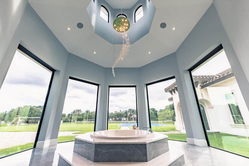 This is a close look at the bathtub area with a bathtub in the middle surrounded by tall glass windows and topped with a tall ceiling.