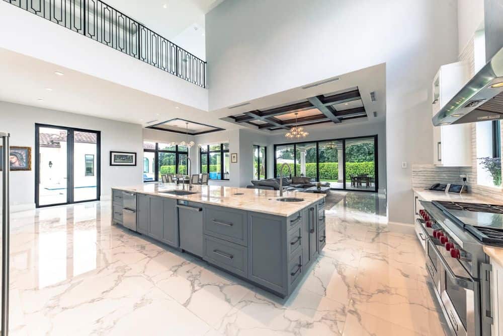 The kitchen area has a large kitchen island that has gray cabinets, drawers and appliances that make it stand out against the marble flooring.