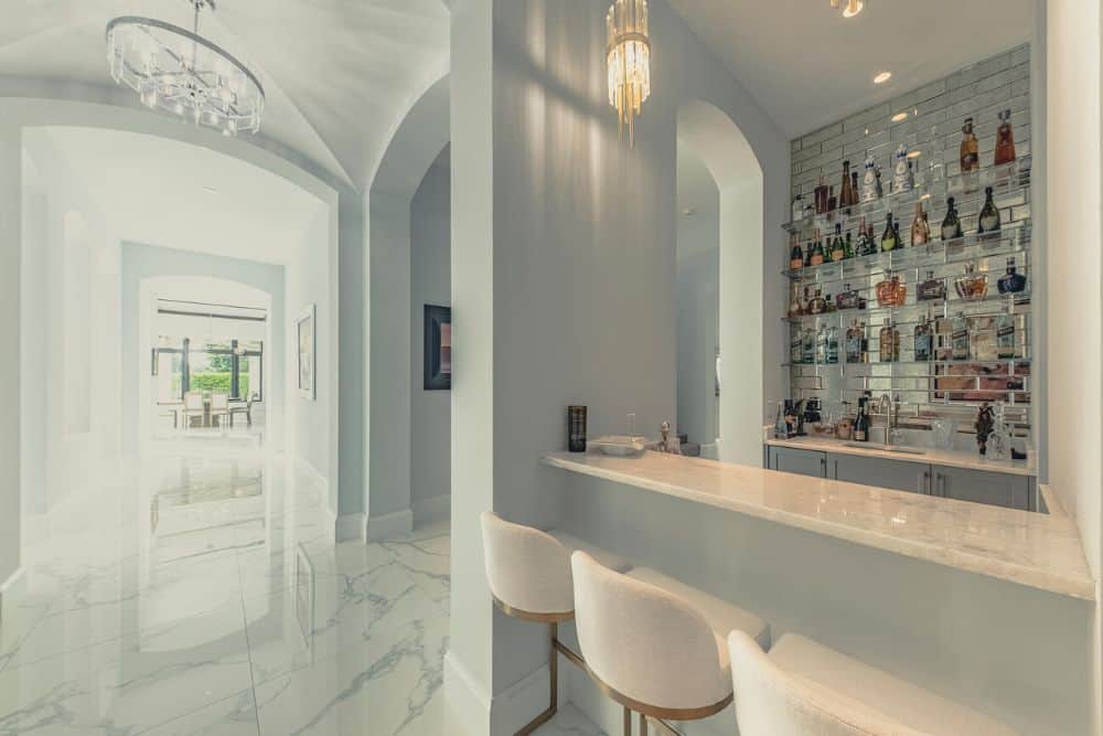 This is a close look at the indoor bar with beige bar stools, beige counter and glass shelves for the liquor storage on the far wall.