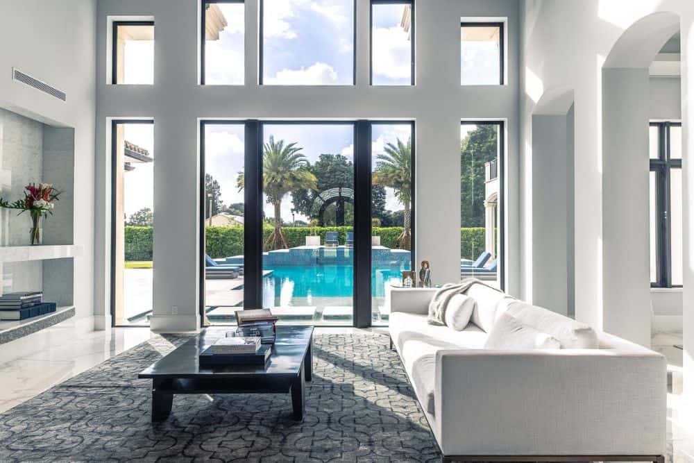 This is a close look at the living room that has tall glass windows on the far side that brings in natural lighting for the sofa and dark coffee table.