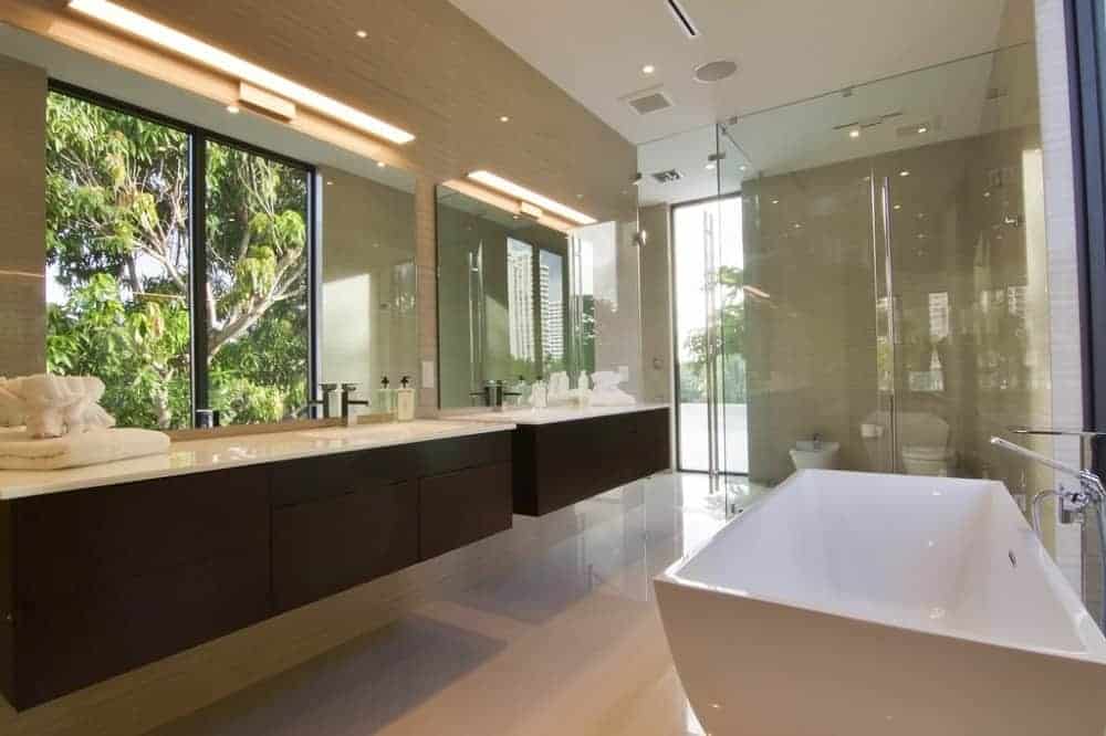 The primary bathroom has a bathtub across from the two-sink floating vanity that has a dark brown tone that contrasts the beige floor and walls.