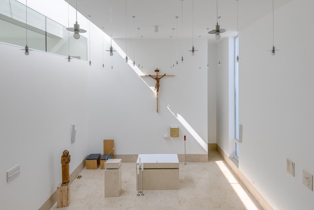 This is another look at the chapel with white walls and beige flooring tiles complemented by the furniture and the wall-mounted crucifix.