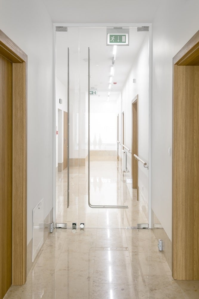 This is a close look at the hallway of the monastery with wooden doors, white walls and wooden handles mounted on the walls after the glass door.