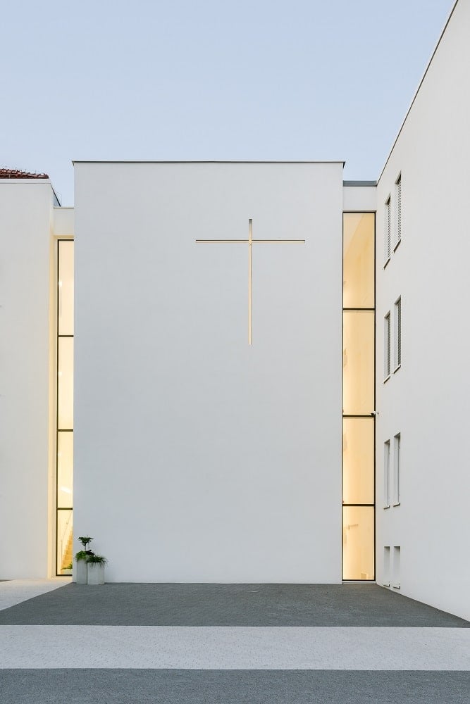 This is a nighttime view of the monastery exterior showcasing the warm lighting from the windows and the crucifix symbol.