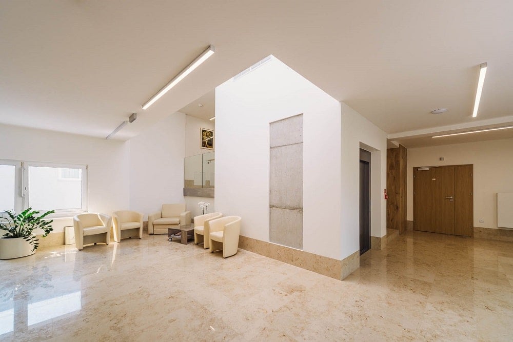 This is a view of the interior showcasing tall beige walls and a collection of beige arm chairs.