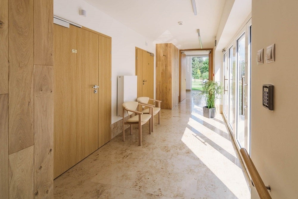 This is a view of the hallway interior with large wooden doors for the rooms and a couple of arm chairs on the side.