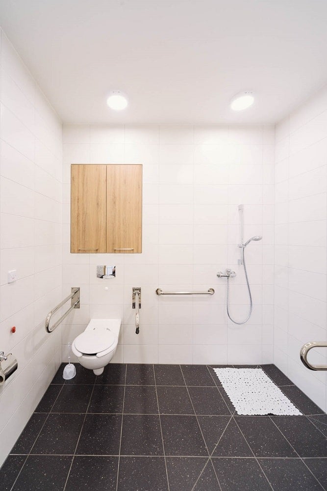 This is the spacious bathroom with hand rails on the sides and black tiles on the floor.
