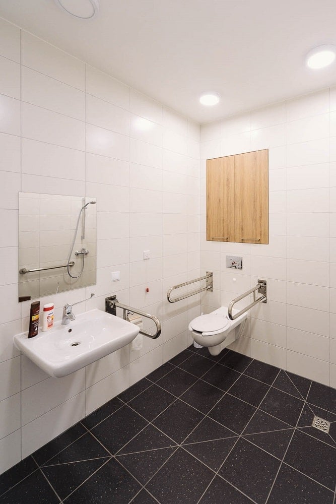 This is another looka t the bathroom showcasing the toilet and floating sink with multiple hand rails on the sides for support.