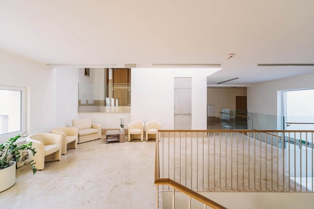 The wide hallway of the interior has a set of arm chairs on the side adorned with potted plants.