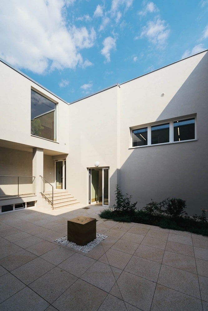 This is the exterior look at the senior house with a small courtyard surrounded by beige exterior walls and windows.