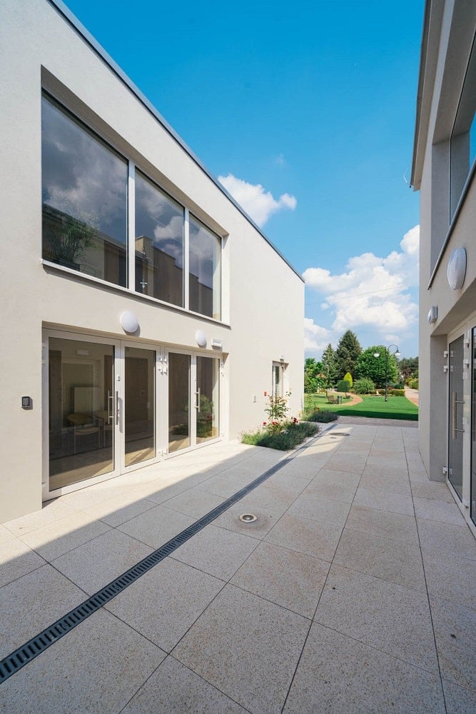 This side of the senior house has large glass windows and doors on both levels adorned with a miniature garden.