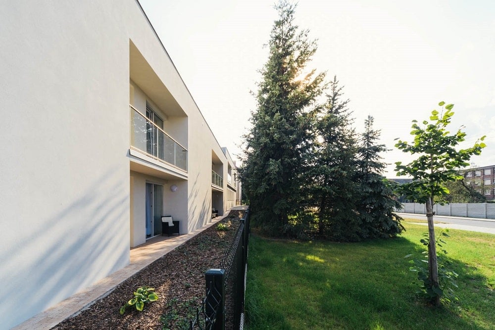 This is closer look at the side of the structure adorned with a garden strip and a few tall trees.