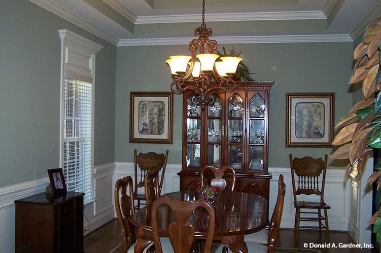 Formal dining room with a tray ceiling, wooden furnishings, and gray walls adorned with white wainscoting and framed artworks.