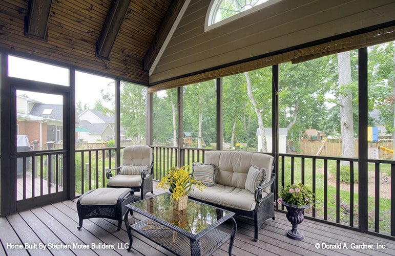 The screened porch is furnished with wicker cushioned seats and a matching glass top coffee table over wide plank flooring.