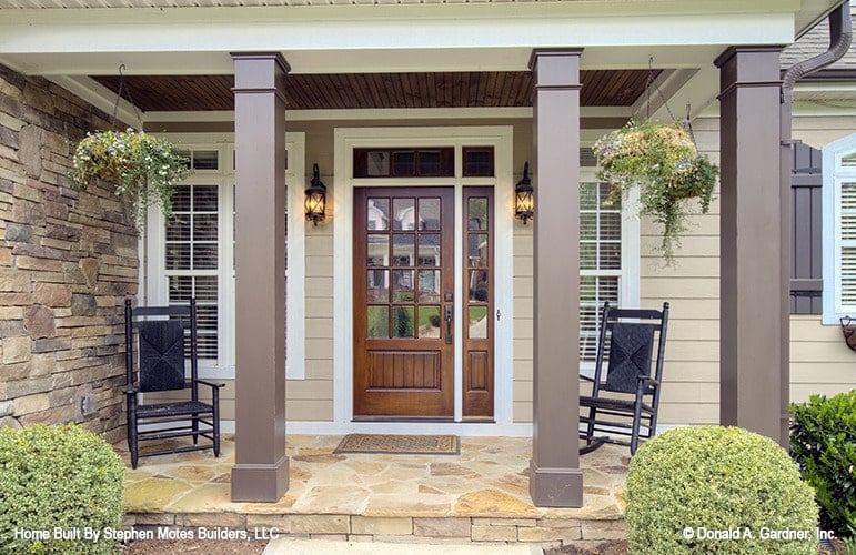 Covered front porch with a black rocker and chair along with a glazed entry door flanked by wall sconces.