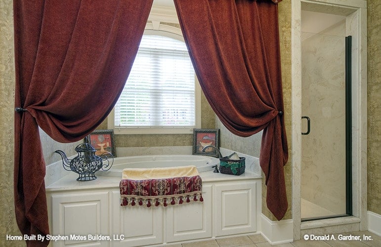 Primary bathroom with a walk-in shower and a deep soaking tub dressed in heavy red draperies.