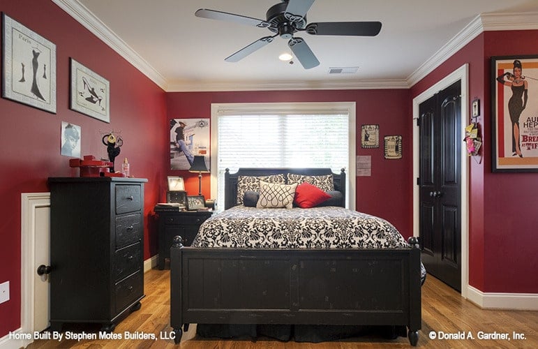 This bedroom has dark wood furnishings, hardwood flooring, and bold red walls lined with white trims.