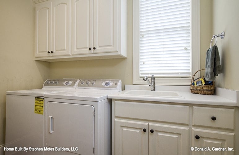 The utility room is equipped with a white washer and dryer, white cabinets, a porcelain sink, and a louvered window.