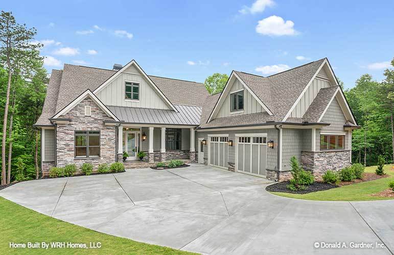 This is a front view of the house that has a large concrete driveway and neutral tones on its exterior walls and roof complemented by the landscape of shrubs and grass as well as tall trees in the background.