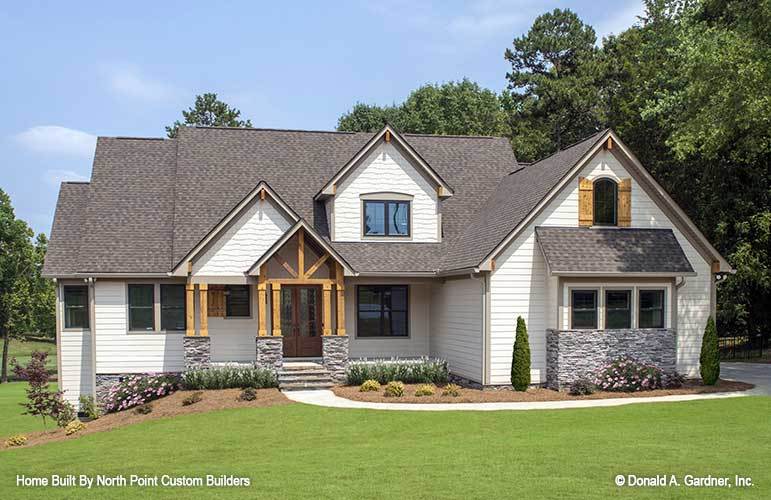This is a view of the front exterior of the house that has a concrete walkway in the middle of a grass lawn and the soil on the side of the house planted with various shrubs to complement the white shiplap walls.