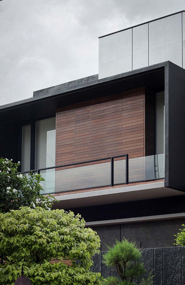 This is a close look at the upper level of the house exterior showcasing the wooden panel and glass railings of the balcony paired iwth frosted glass doors from the bedroom.