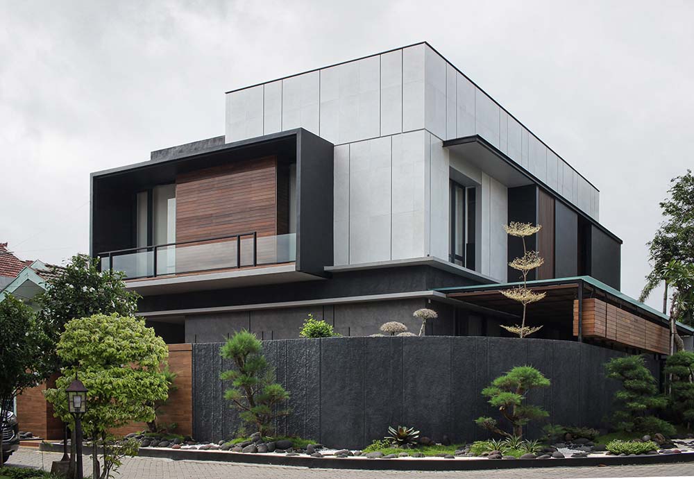 This is a full view of the house with tall dark gray fences surrounding the property adorned with tall shrubs and trees.