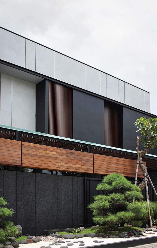 This side of the house exterior has dark and tall fences that is topped with wooden elements and adorned with various medium-sized trees and shrubs.