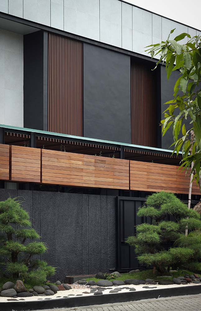 The landscaping of medium-sized trees and shrubs complement the dark gray outer walls of the house.
