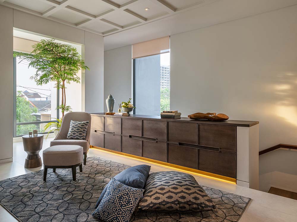 This is a close look at the reading nook and play area that has a large patterned area rug and a comfortable cushioned chair by the glass wall.