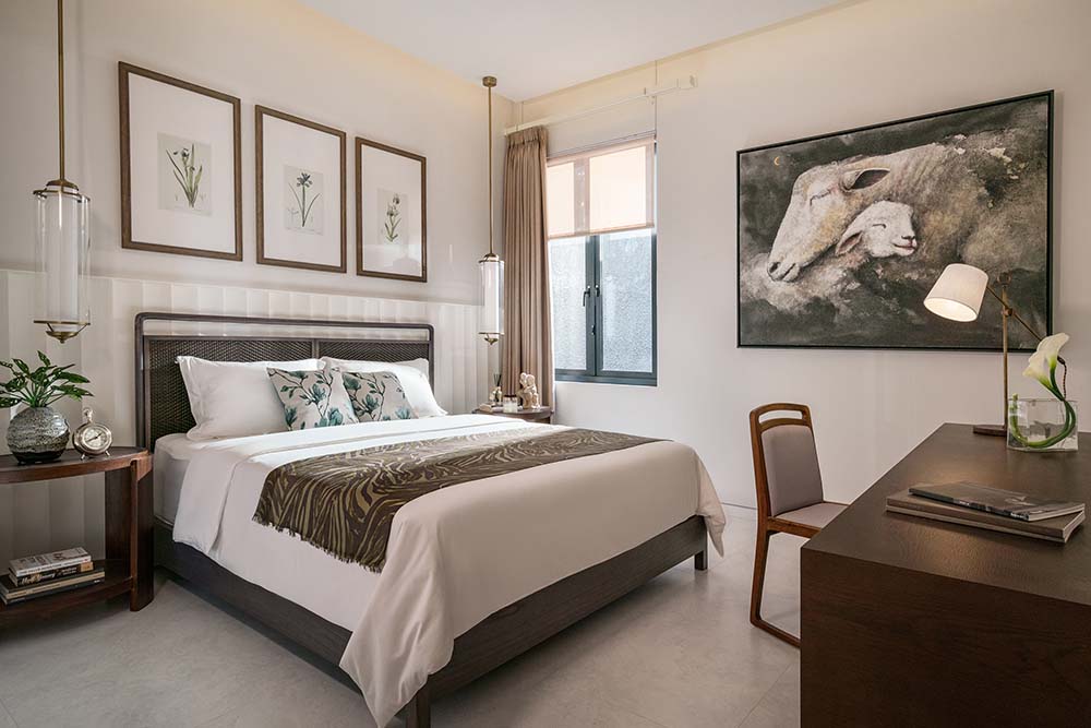 This bedroom has a large gray bed adorned with multiple wall-mounted artworks on the beige walls.