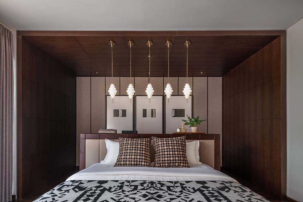 This is a closer look at the alcove of the bed headboard with dark wooden planks and pendant lights above the headboard.