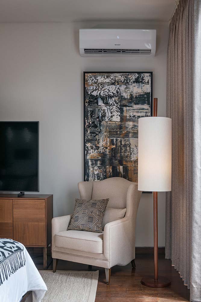 Across from the bed is the beige armchair on the corner beside the standing lamp and the TV on a wooden cabinet.