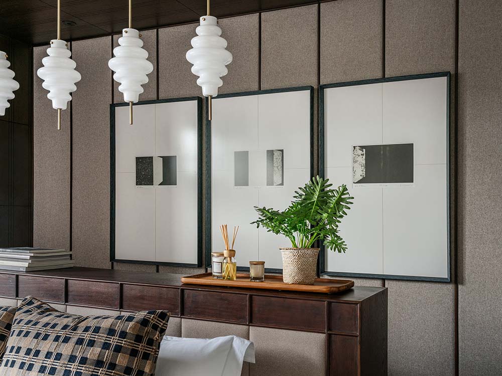 This is a closer look at the bed's dark wooden headboard complemented by the pendant lights from above and the wall-mounted artworks.