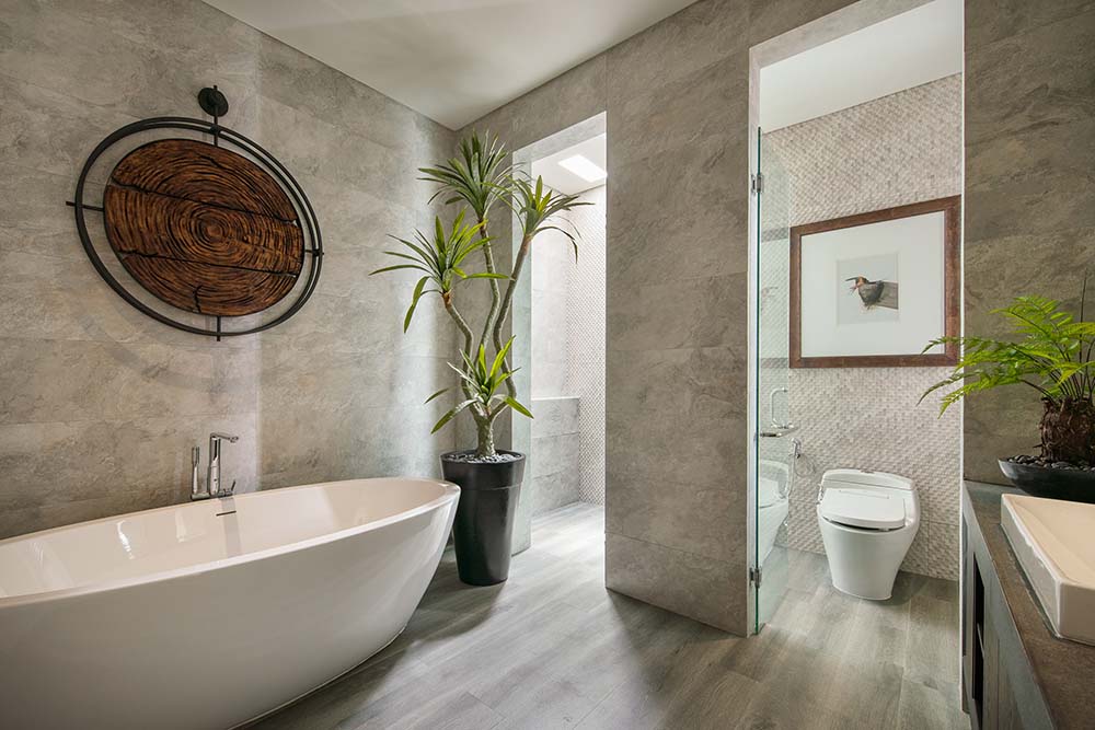The bathroom has a freestanding white porcelain bathtub on the other side adorned with a potted plant by the walk-in shower area.