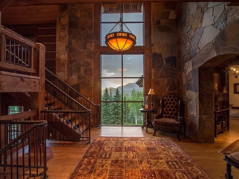 Upon entry into the house, you are welcomed by this foyer with mosaic stone walls that go well with the hardwood flooring, wrought-iron railings, and wooden steps of the staircase. These are then topped with a tall ceiling that hangs a pendant light over the patterned area rug.