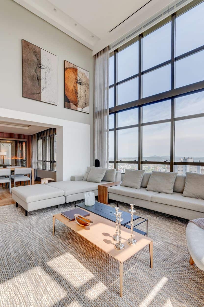 This is a full view of the living room with a large L-shaped sofa and a couple of coffee tables complemented by the wall artworks and large glass wall.