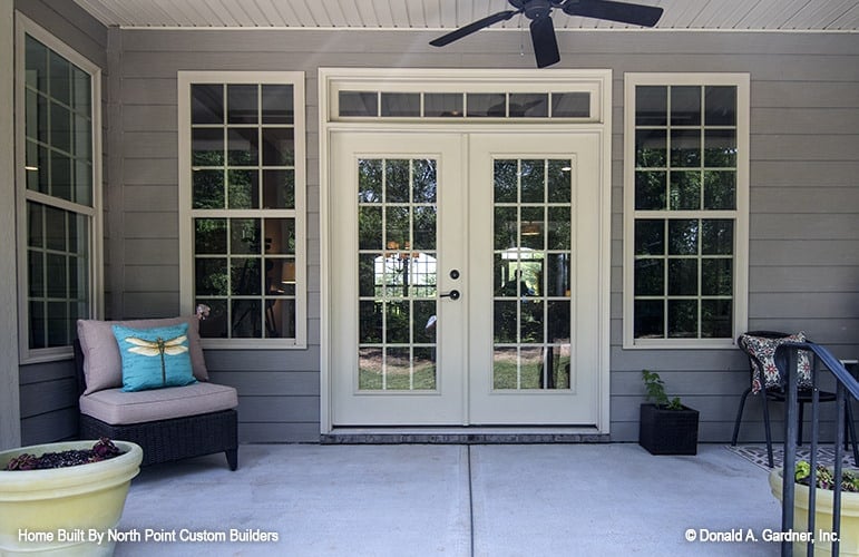 The covered porch is filled with round back chairs, a wicker lounge chair, and potted plants.