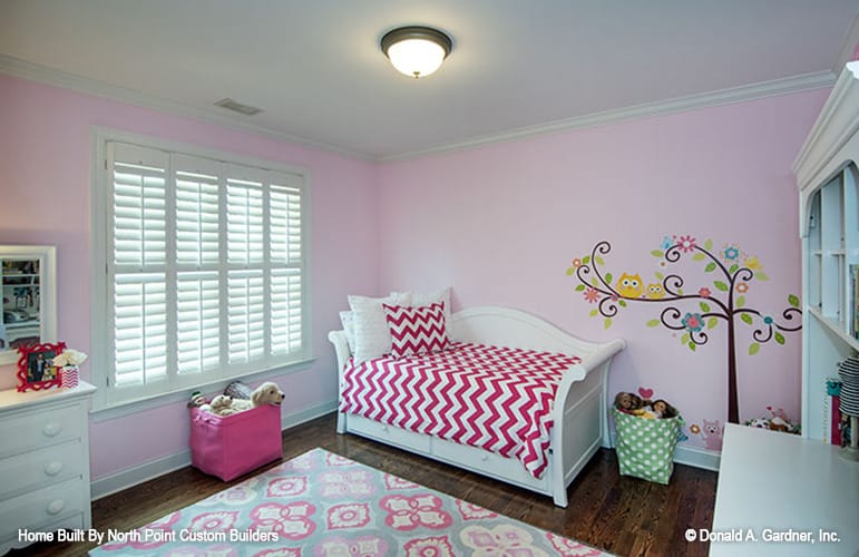 Another kid's bedroom with pink walls, a patterned rug, and a daybed dressed in a red chevron blanket.