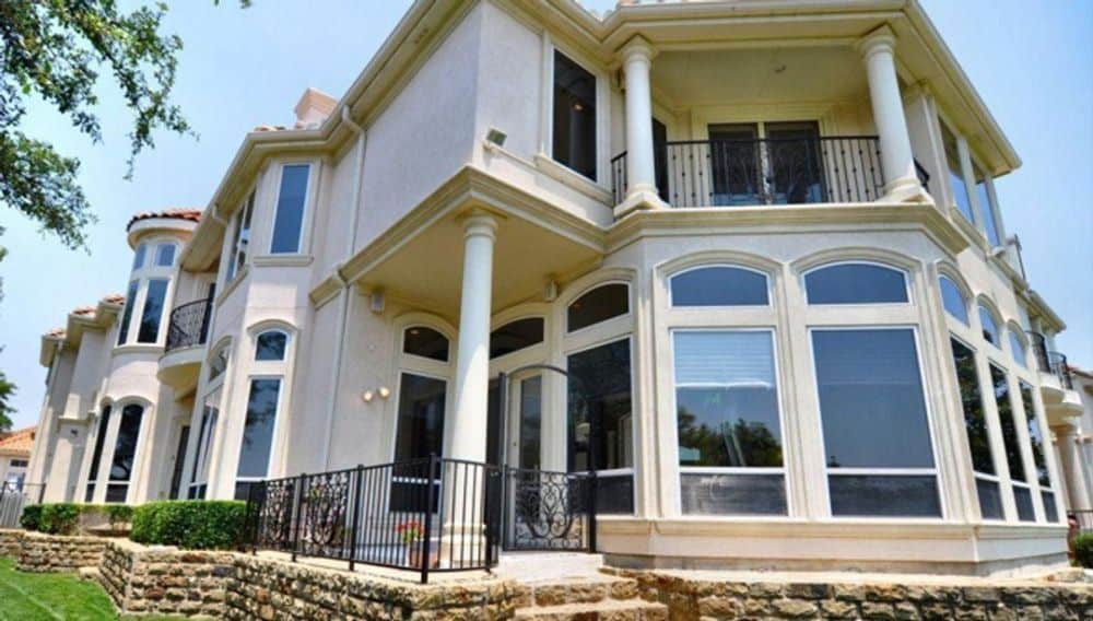 Rear exterior view with arched windows, an upper balcony, and a covered porch lined with a column.