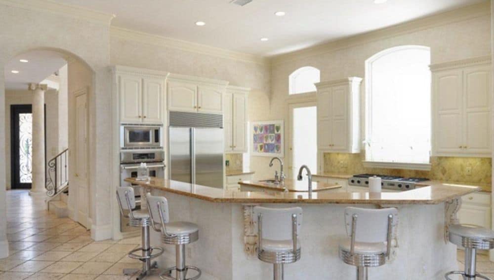 The kitchen offers white cabinetry, a center island, and a curved eating bar paired with round stools.