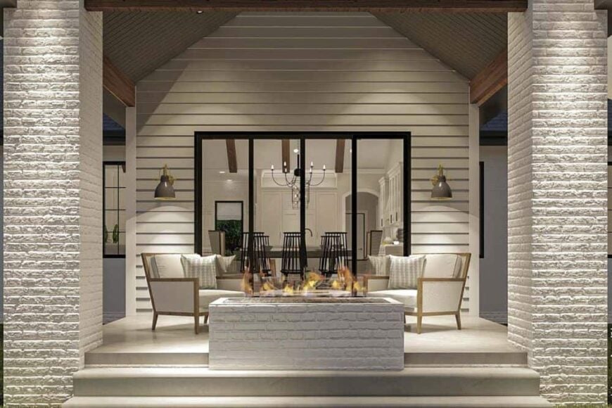 Rear covered porch with white cushioned seats and a brick fire pit over concrete flooring.