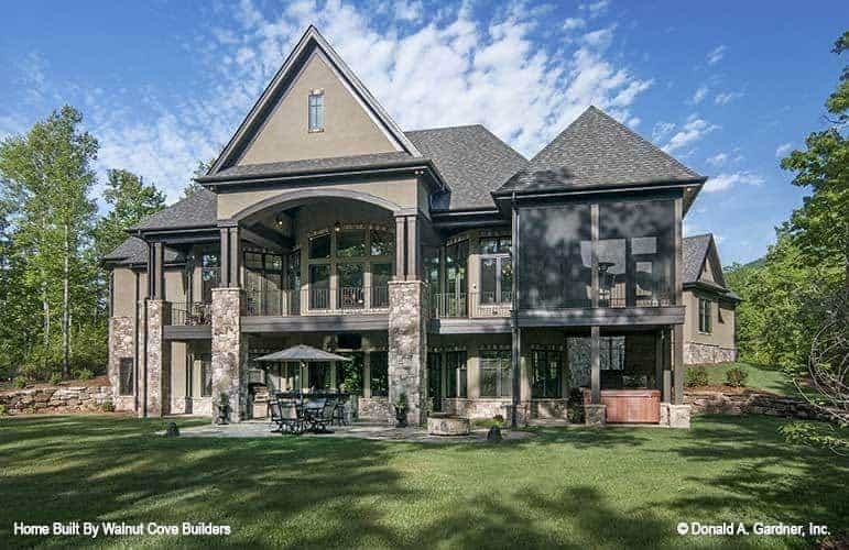 This is an exterior view of the back of the house that has mosaic stone flooring on its outdoor patio areas before transitioning to a grass lawn with tall trees on the sides.
