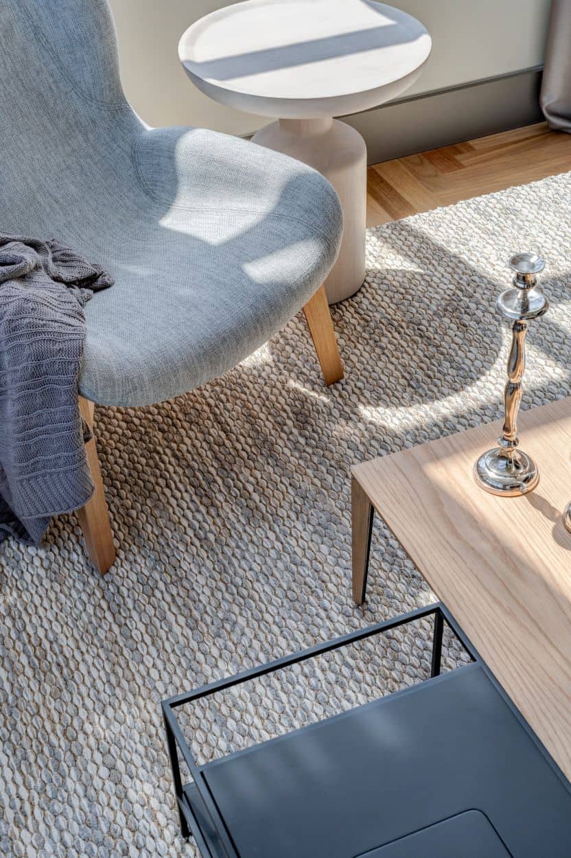 This is a close look at the living room coffee tables and the gray chair beside it that serves as a reading nook on the gray area rug that covers most of the hardwood flooring.