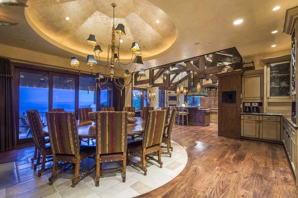 This is the formal dining room with a large wooden circular dining table topped with a decorative chandelier from a dome ceiling. These are then complemented by the hardwood flooring.