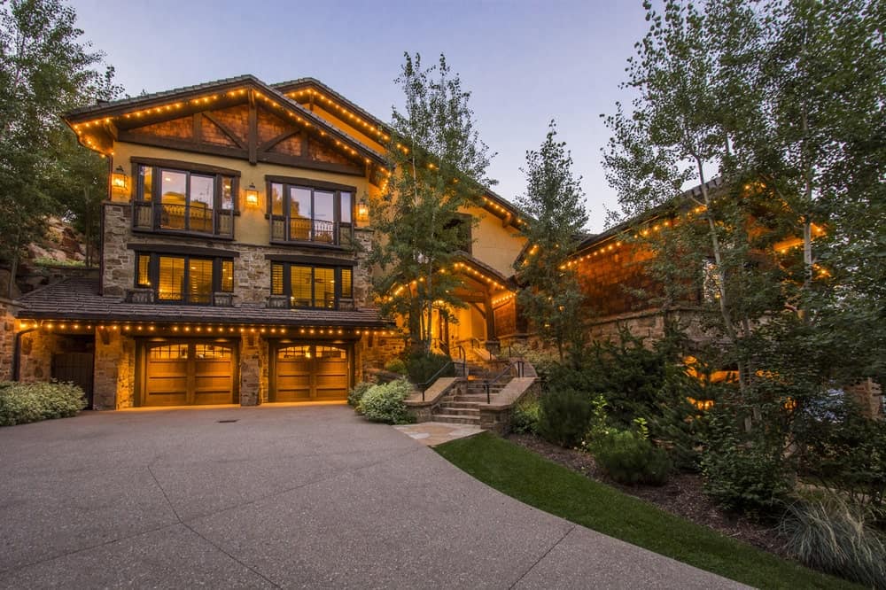 This is a front view of the house from the vantage of the driveway. This lets you appreciate the warm glow of the glass walls of the house. These are complemented by the landscaping of tall tree and thick shrubs.