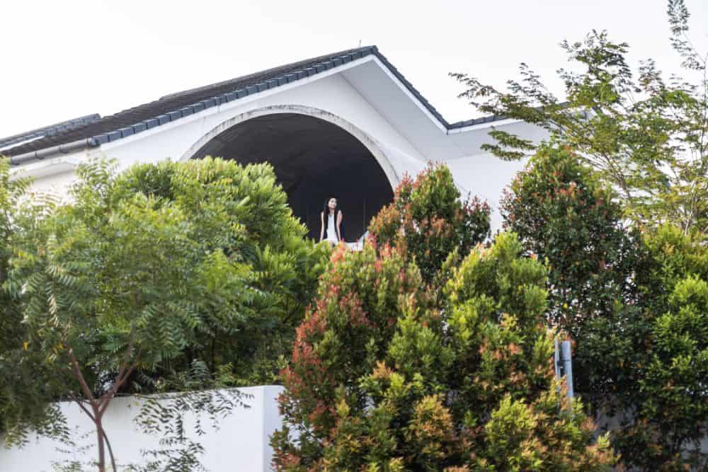 This is an exterior view of the house with bright exterior walls complemented by the surrounding lush landscape of trees and shrubs.
