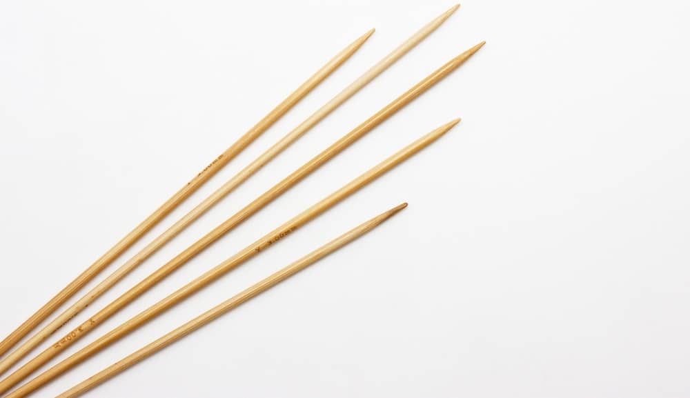 This is a close look at various straight knitting needles on a white surface.