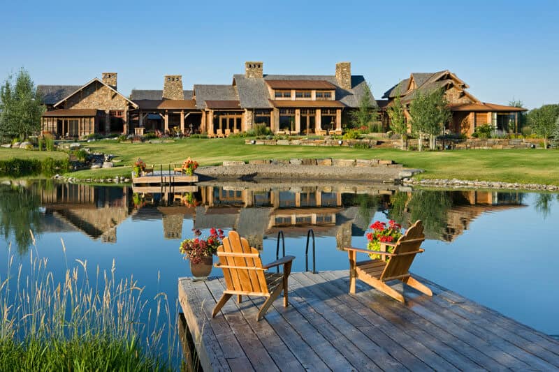 This is a full view of the back of the house that has a alrge grass lawn, thick shrubs and a large pond surrounded by decorative rocks.